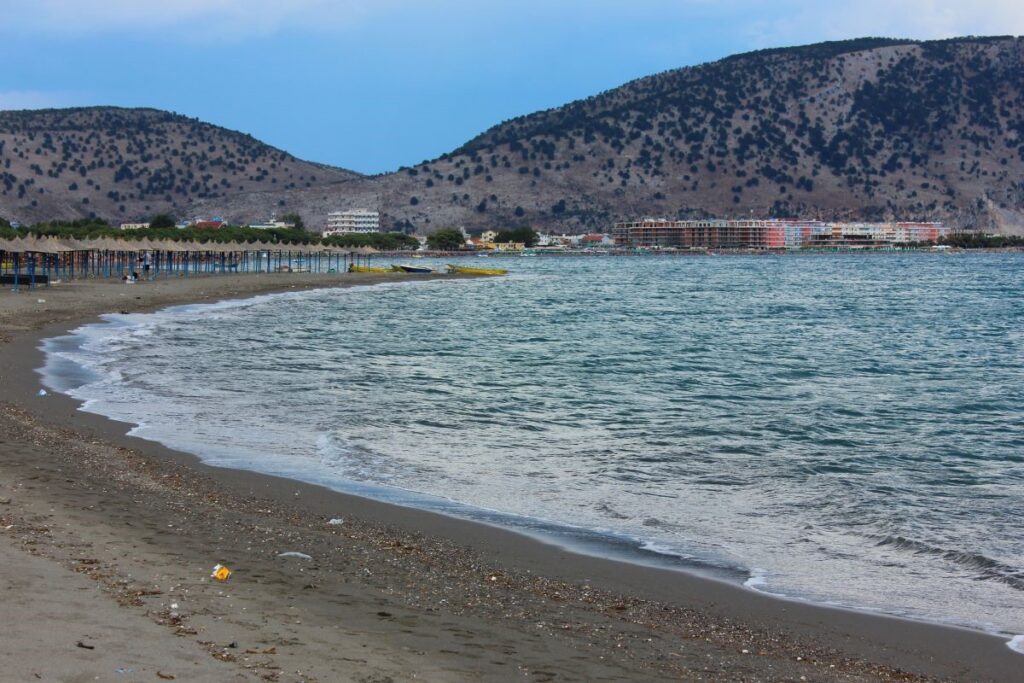 Beach with calm waves, shaded umbrellas, and distant hills in northern Albania