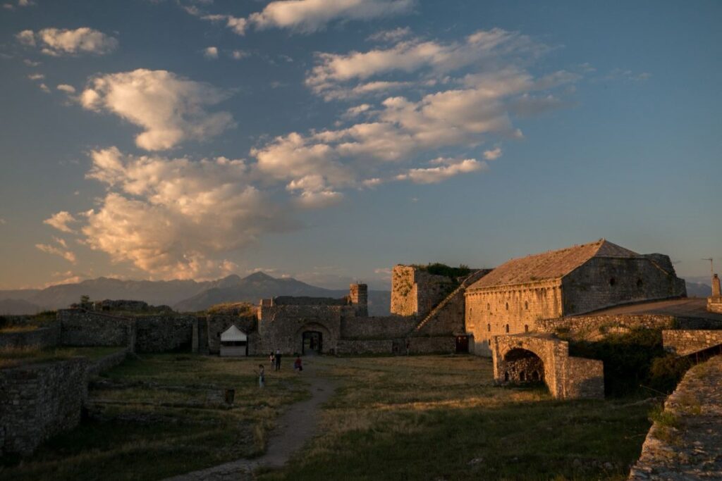 Rozafa Castle at sunset with Lake Shkodër and the surrounding mountains in the background.