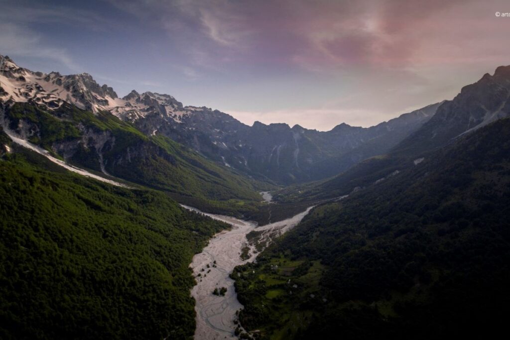 Valbona Valley in North Albania, featuring rugged mountain peaks and lush greenery under a clear blue sky.