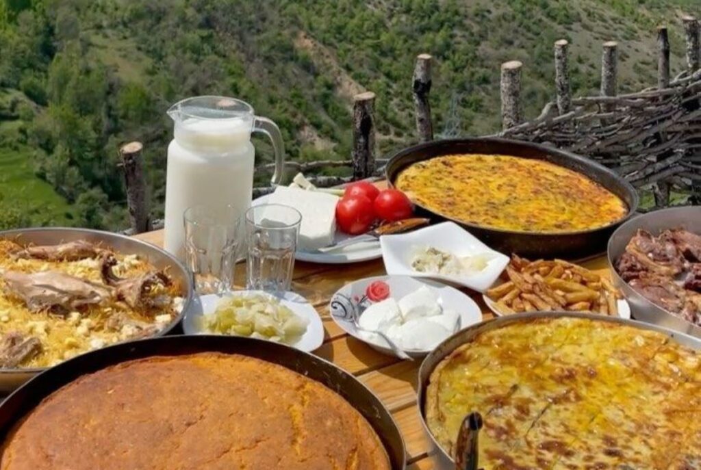 A colorful spread of traditional Albanian dishes including Tavë Kosi, byrek, and qifqi on a rustic wooden table.