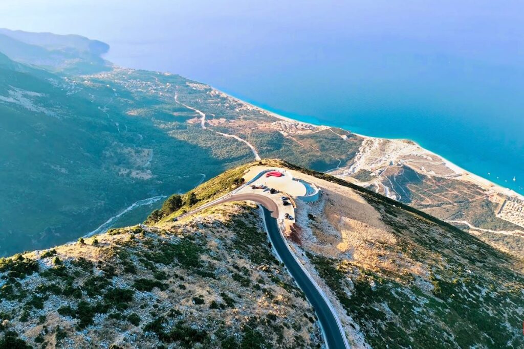 A scenic view of the Llogara Pass, with winding roads and lush greenery leading to the Ionian Sea.