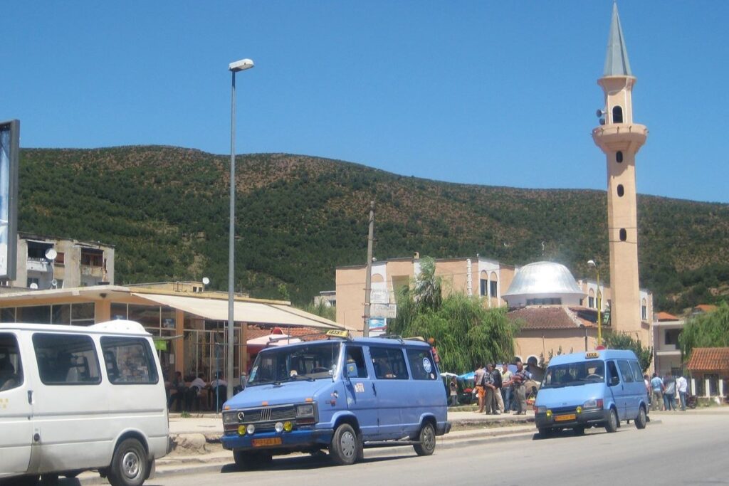 A furgon, a traditional Albanian minibus, parked with a scenic mountain view in the background.