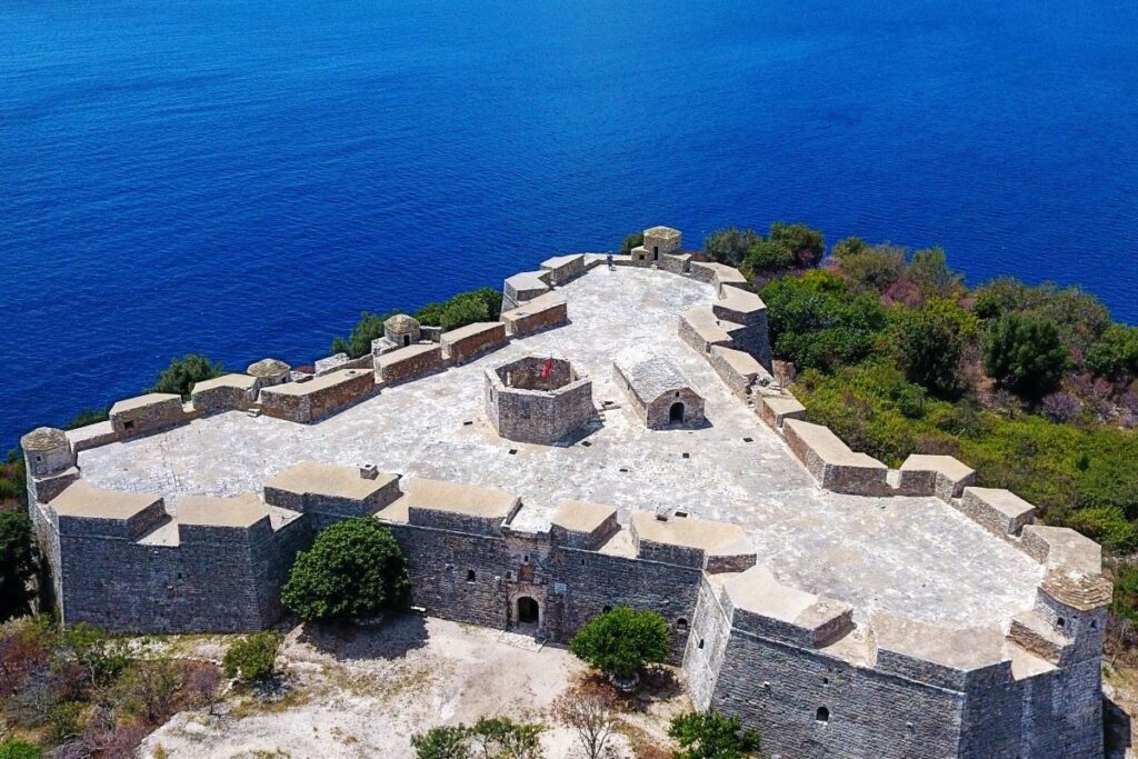 Porto Palermo Castle perched on a peninsula with turquoise Ionian Sea waters in the background.