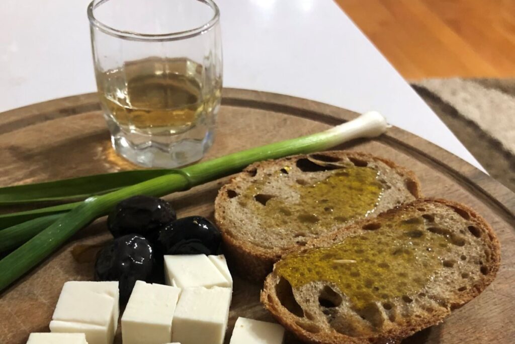 Traditional Albanian Raki served with olives, cheese, and bread on a rustic table.