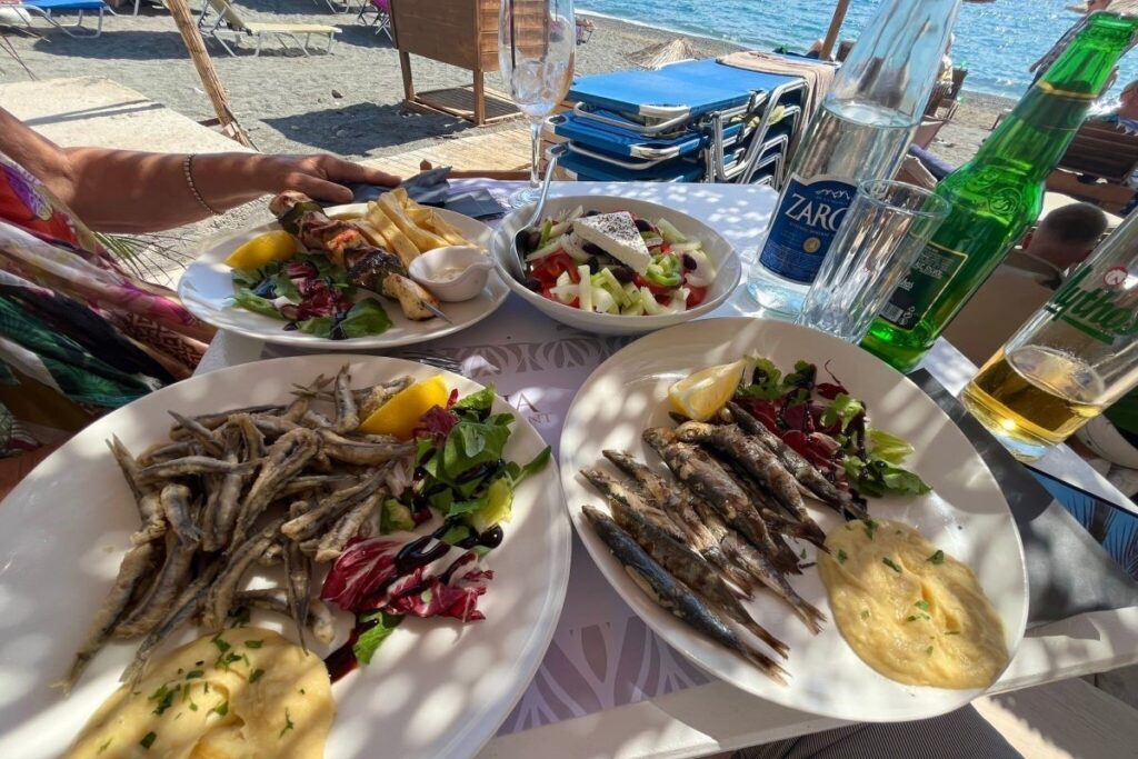 A table filled with grilled seafood, olive oil, and wine overlooking the turquoise Ionian Sea in South Albania.