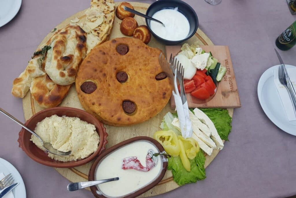 A traditional Albanian meal featuring fërgesë, byrek, and tavë dheu with raki on the side.