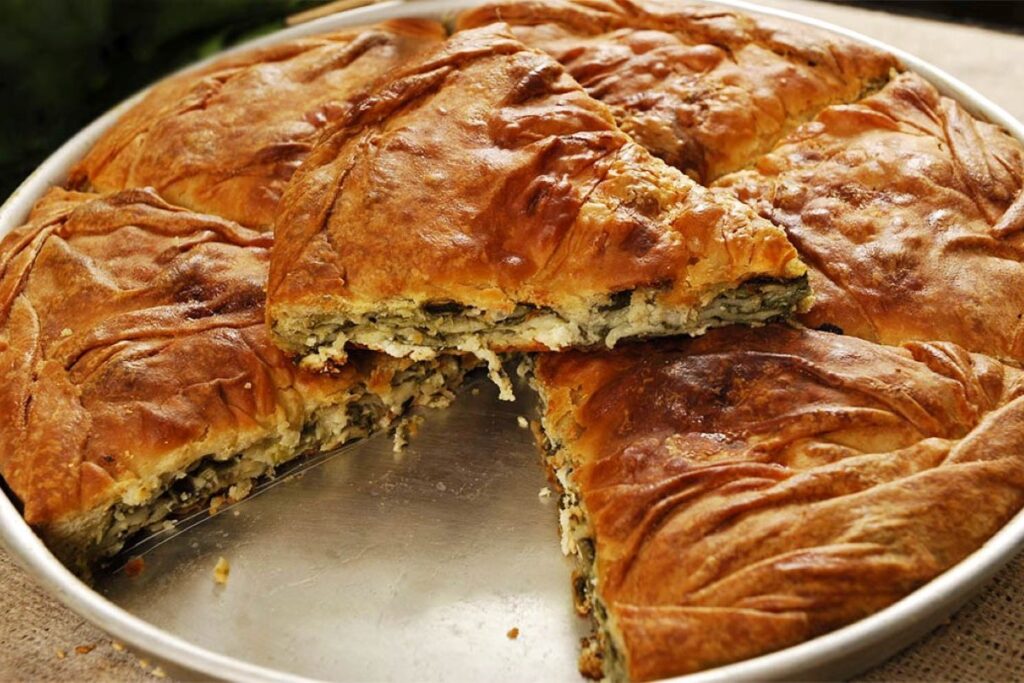 A table filled with traditional Albanian dishes including Tavë Kosi and byrek.