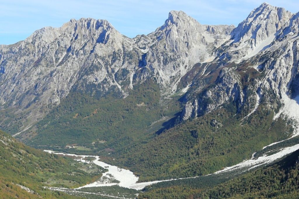 A hiker standing on a trail in Valbona Valley, Albania, surrounded by dramatic mountain scenery.