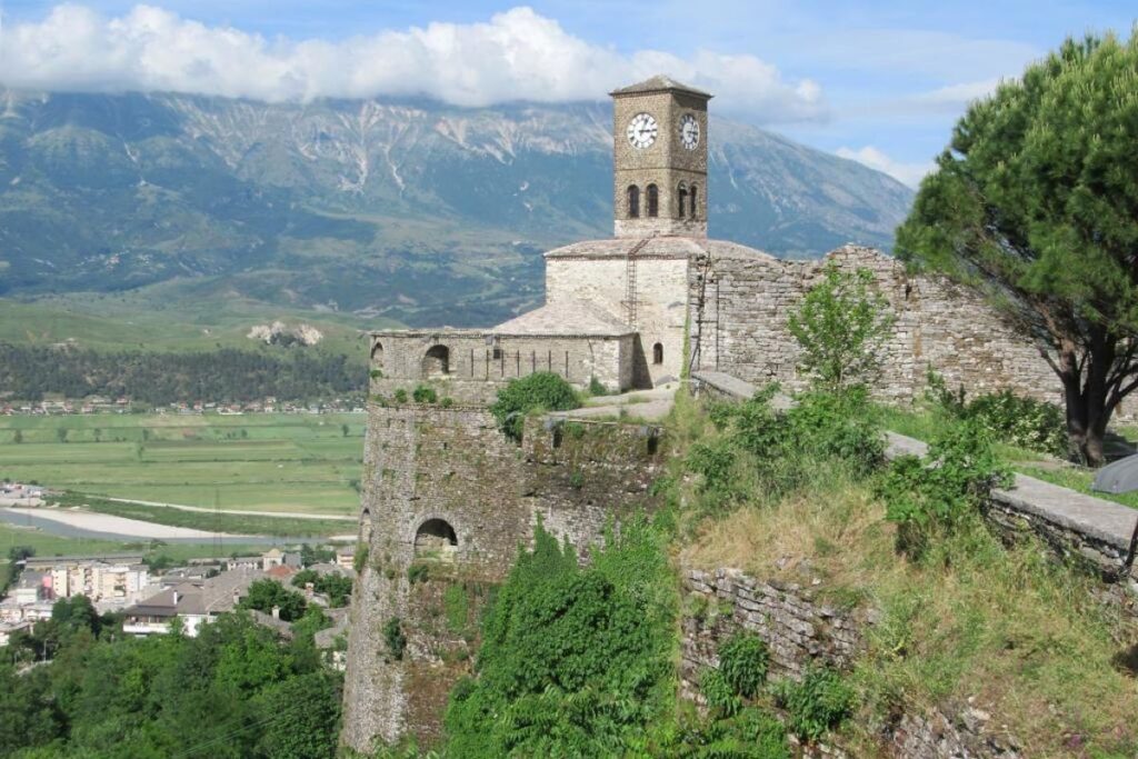 Gjirokastër Castle sitting high above the stone-roofed city with stunning mountain views in the background.