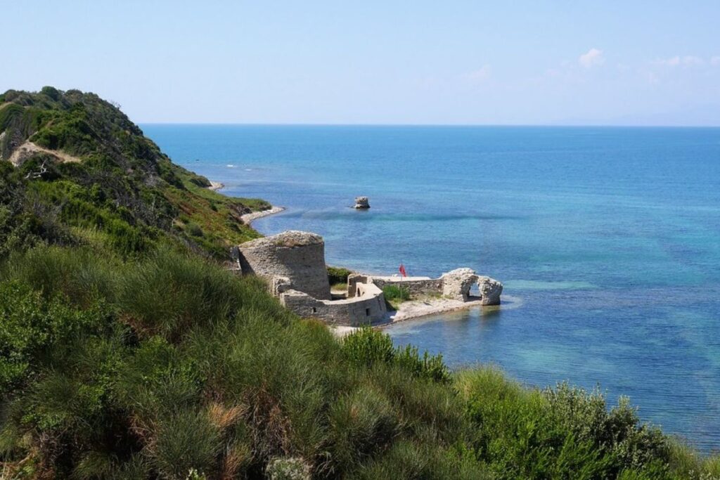 Rodoni Castle ruins perched above the Adriatic Sea, surrounded by lush greenery and a tranquil coastline.