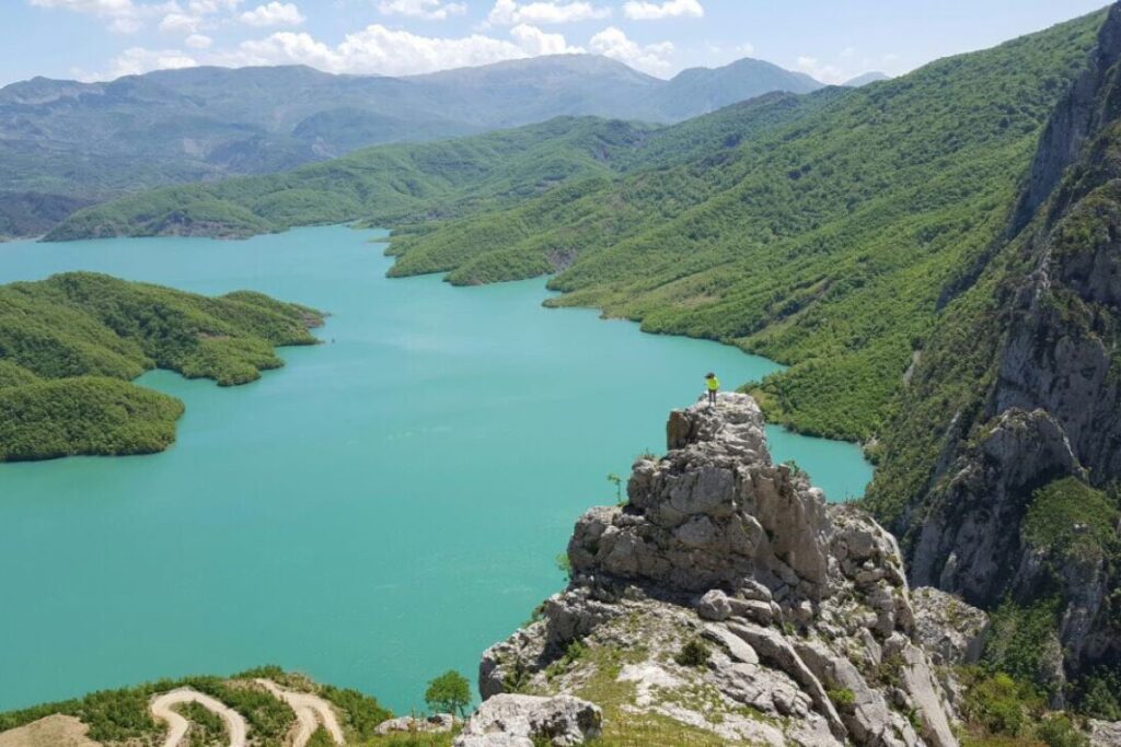 Bovilla Reservoir with turquoise waters surrounded by cliffs and lush greenery under a bright blue sky.