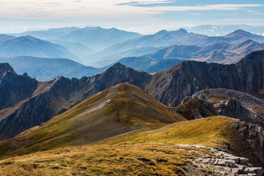 Mount Korab’s towering peak surrounded by green valleys and clear blue skies, viewed from a hiking trail.