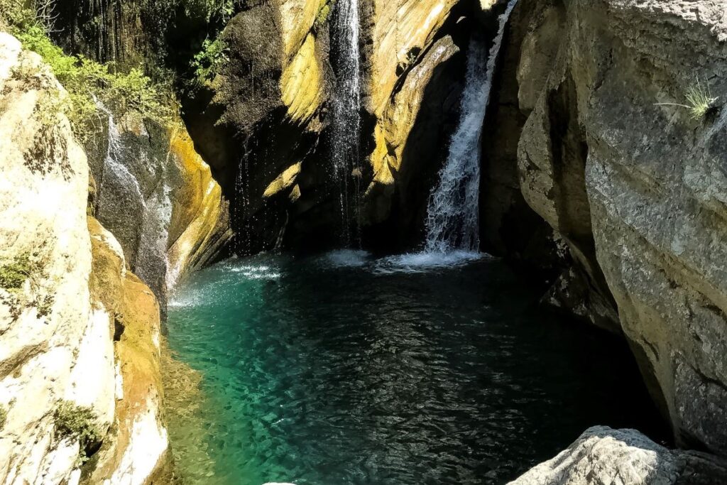 Waterfall flowing into a turquoise pool surrounded by greenery and rocky cliffs