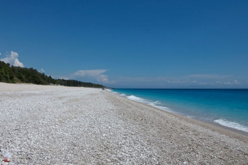 Dhërmi Beach with clear turquoise waters and lush green hills along the Albanian Riviera.