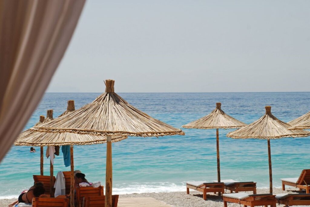 Dhërmi Beach with turquoise waters, white pebbles, and green hills on the Albanian Riviera.