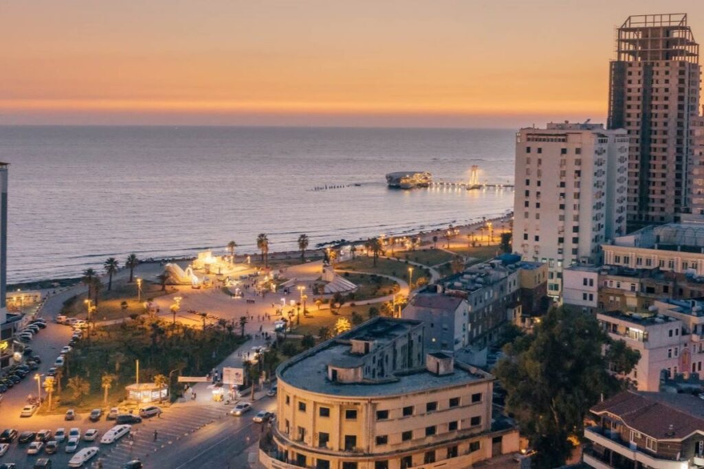 The scenic Vollga promenade in Durrës, with palm trees and a view of the Adriatic Sea at sunset.