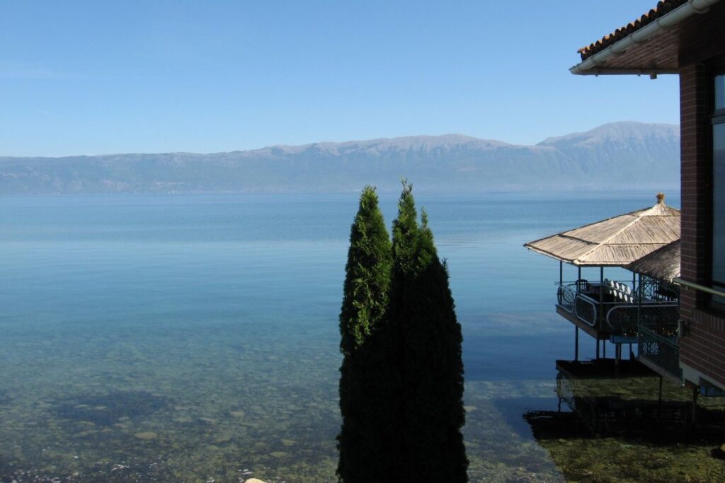 Lake Ohrid at sunrise, with reflections of the surrounding mountains on its calm waters.